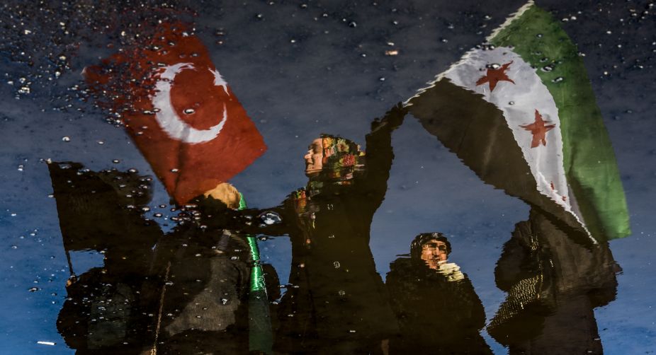 A reflection on waste liquid shows a woman wawing Turkish and Free Syrian flags as an aid convoy to Aleppo organized by IHH Humanitarian Relief Foundation is about to leave in Istanbul (Photo: Ozan Kose/AFP) img