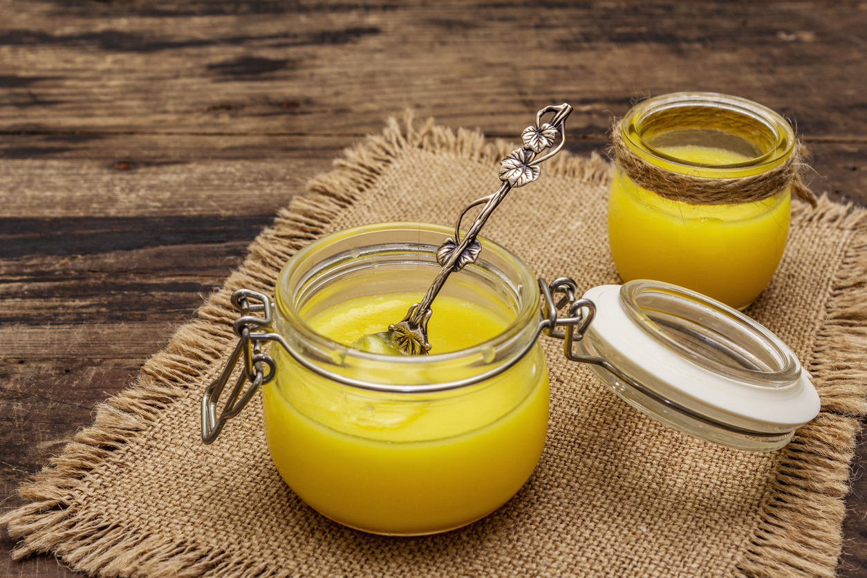 Pure or desi ghee (ghi), clarified melted butter. Healthy fats bulletproof diet concept or paleo style plan. Glass jars, silver spoon on vintage sackcloth. Wooden boards background, copy space