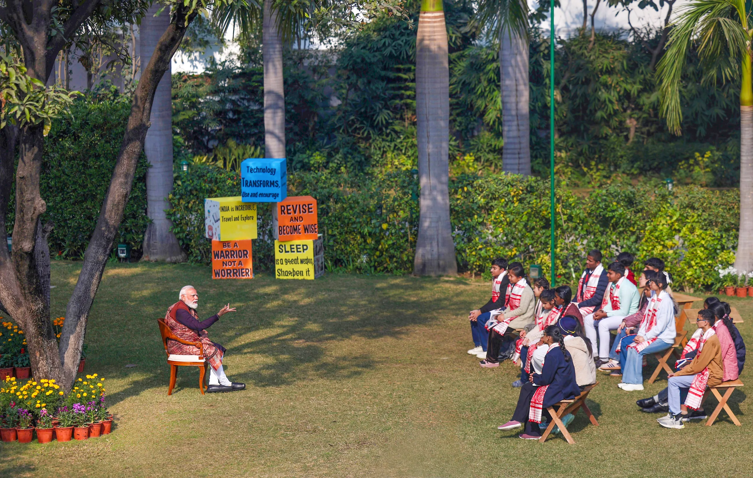 The Prime Minister engages in a lively conversation with students seated in an open-air classroom setting. img