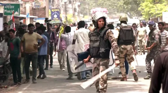 CAPF personnel holding shields and batons manage crowd during election-related unrest in West Bengal.